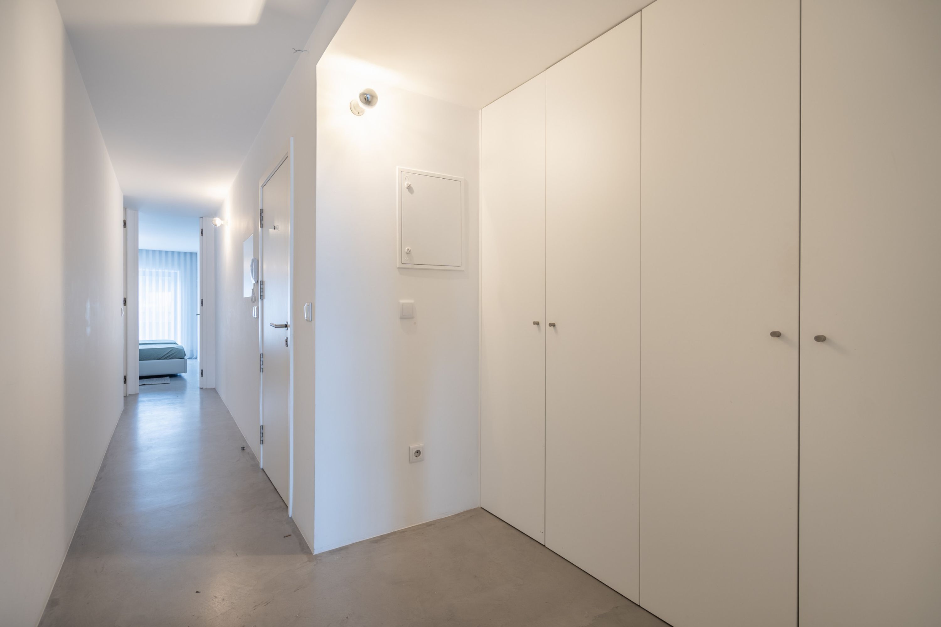 Ein Flur mit einem Bett in der Ferne, einem Kleiderschrank und einem Lichtschalter an der Wand.