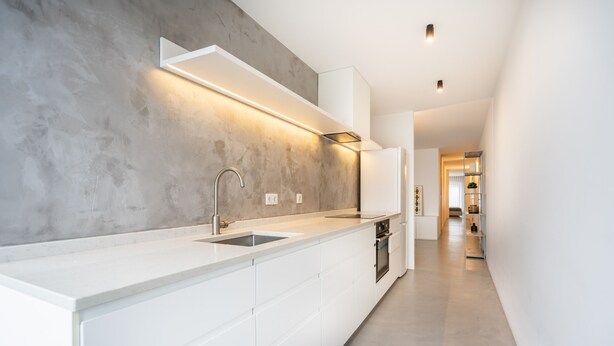 Una cucina moderna con piano di lavoro bianco, lavello in acciaio inossidabile e schienale grigio.