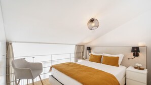 A modern bedroom with a large bed, a chair, a nightstand, and a wall-mounted lamp. - Souto Essence Apartment By Minhos Guest (Braga)