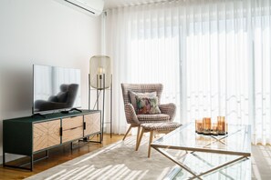 Un salon moderne avec un téléviseur à écran plat, un fauteuil en osier, une table basse en verre et un lampadaire.