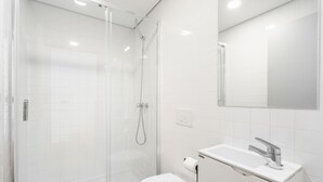 A modern bathroom with a glass-enclosed shower, a white toilet, and a sink with a mirror above it. - Souto Essence Apartment By Minhos Guest (Braga)