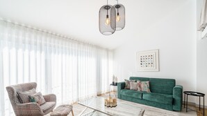 A living room with a green sofa, a patterned armchair, a glass coffee table, and a black side table. - Souto Essence Apartment By Minhos Guest (Braga)