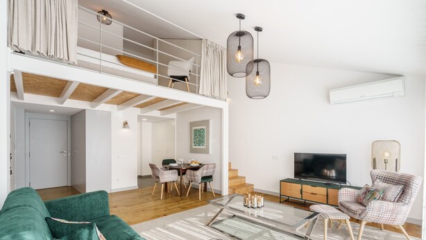 A spacious living room with a green sofa, a glass coffee table, and a TV. There is a dining area with a table and chairs, and a staircase leading to a loft. - Souto Essence Apartment By Minhos Guest (Braga)
