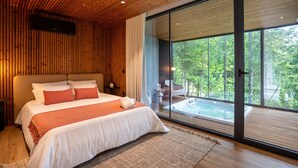 Ein modernes Schlafzimmer mit einem großen Bett, einer Glastür, die auf einen Balkon mit Whirlpool führt, und einer Holzbalkendecke.