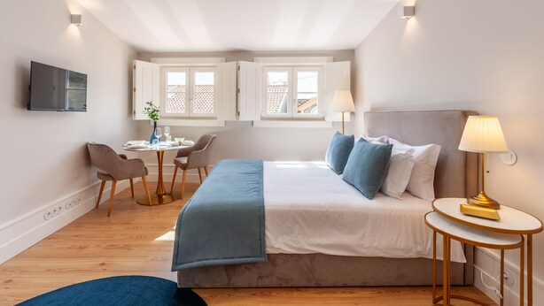 A modern bedroom with a bed, bedside table, lamp, and a dining area with chairs and a table. - Living Valverde Studio Azul - Minho s Guest (Braga)