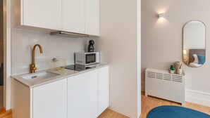 A compact kitchen with white cabinets, a stainless steel range hood, a microwave, and a coffee maker. - Living Valverde Studio Azul - Minho s Guest (Braga)