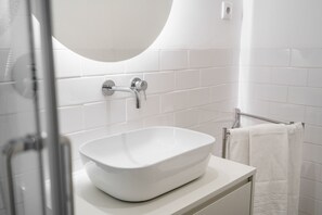 A modern bathroom with a white sink, a round mirror, and a glass shower enclosure. - Porta 120 S o Vicente by Minho s Guest (Braga)
