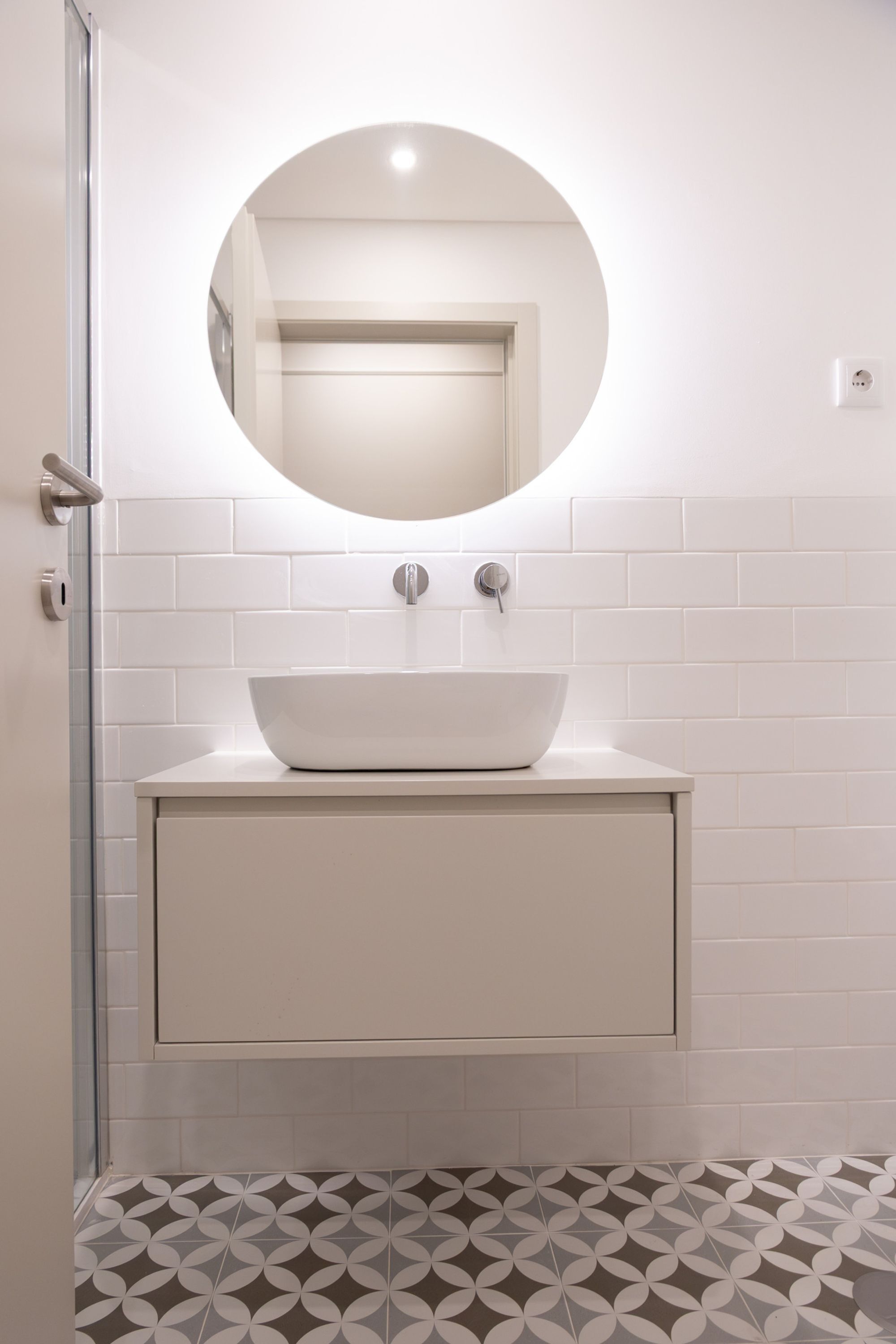 Un baño con un lavamanos blanco, un espejo redondo y un suelo con diseño.