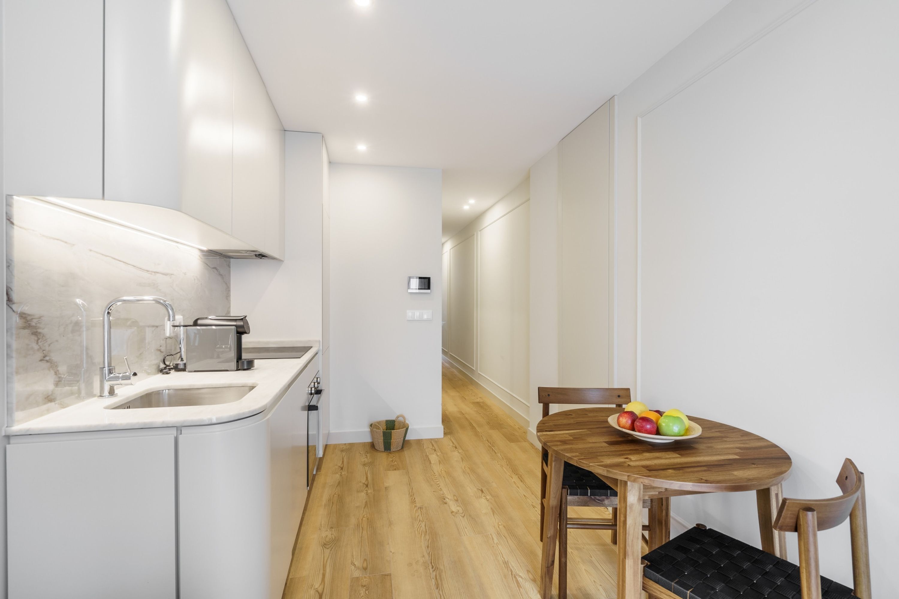 A modern kitchen with white cabinets, a marble countertop, and a wooden dining table with chairs.