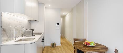 A modern kitchen with white cabinets, a marble countertop, and a wooden dining table with chairs.