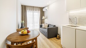 A modern living room with a grey sofa, a wooden dining table with fruit, and a kitchen area with a sink and cabinets. - Porta 120 S o Vicente by Minho s Guest (Braga)