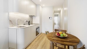 A modern kitchen with white cabinets, a marble backsplash, and a wooden dining table with a fruit bowl. - Porta 120 S o Vicente by Minho s Guest (Braga)