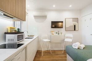 A compact hotel room with a kitchenette, a bed with green bedding, a flat-screen TV, and a mirror on the wall. - Liberty Braga Apartment by Minho s Guest (Braga)