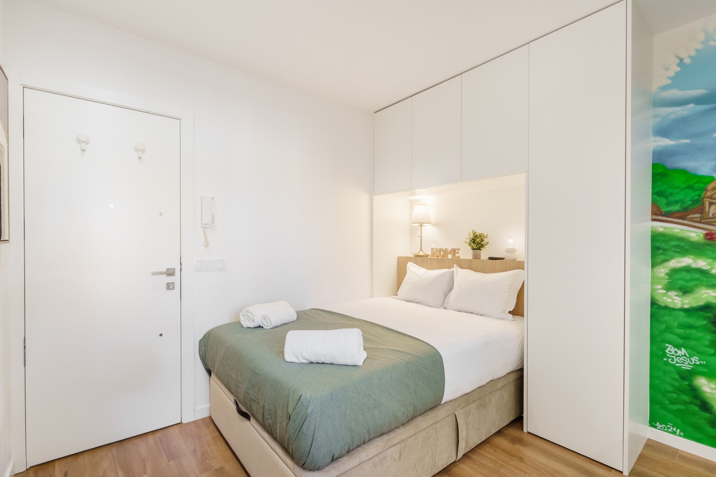 A modern bedroom with a bed, a nightstand, a lamp, and a painting on the wall.