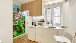 A compact kitchen with a microwave, toaster, and sink. There's a small refrigerator and a window with a view. - Liberty Braga Apartment by Minho s Guest (Braga)