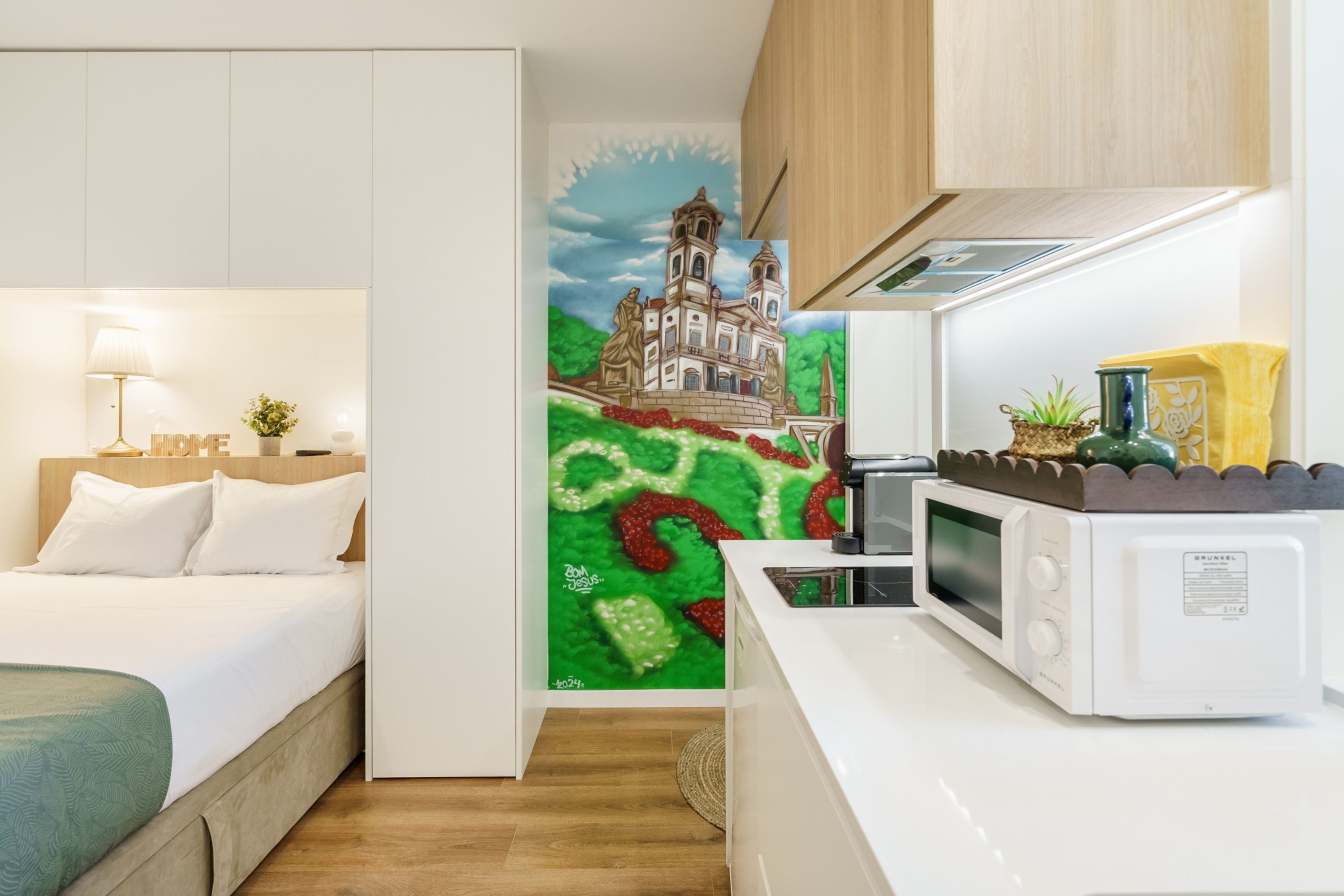 A compact hotel room with a bed, bedside lamp, and a microwave in the kitchenette.