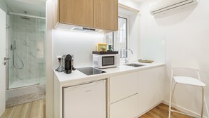 A modern kitchen with white cabinetry, a microwave, a sink, and a glass shower enclosure. - Liberty Braga Apartment by Minho s Guest (Braga)