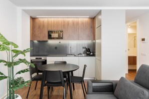 A modern kitchen with wooden cabinets, a stainless steel refrigerator, and a dining area with a round table and black chairs. - 196 Andrade Corvo Apartment by Minho s Guest (Braga)