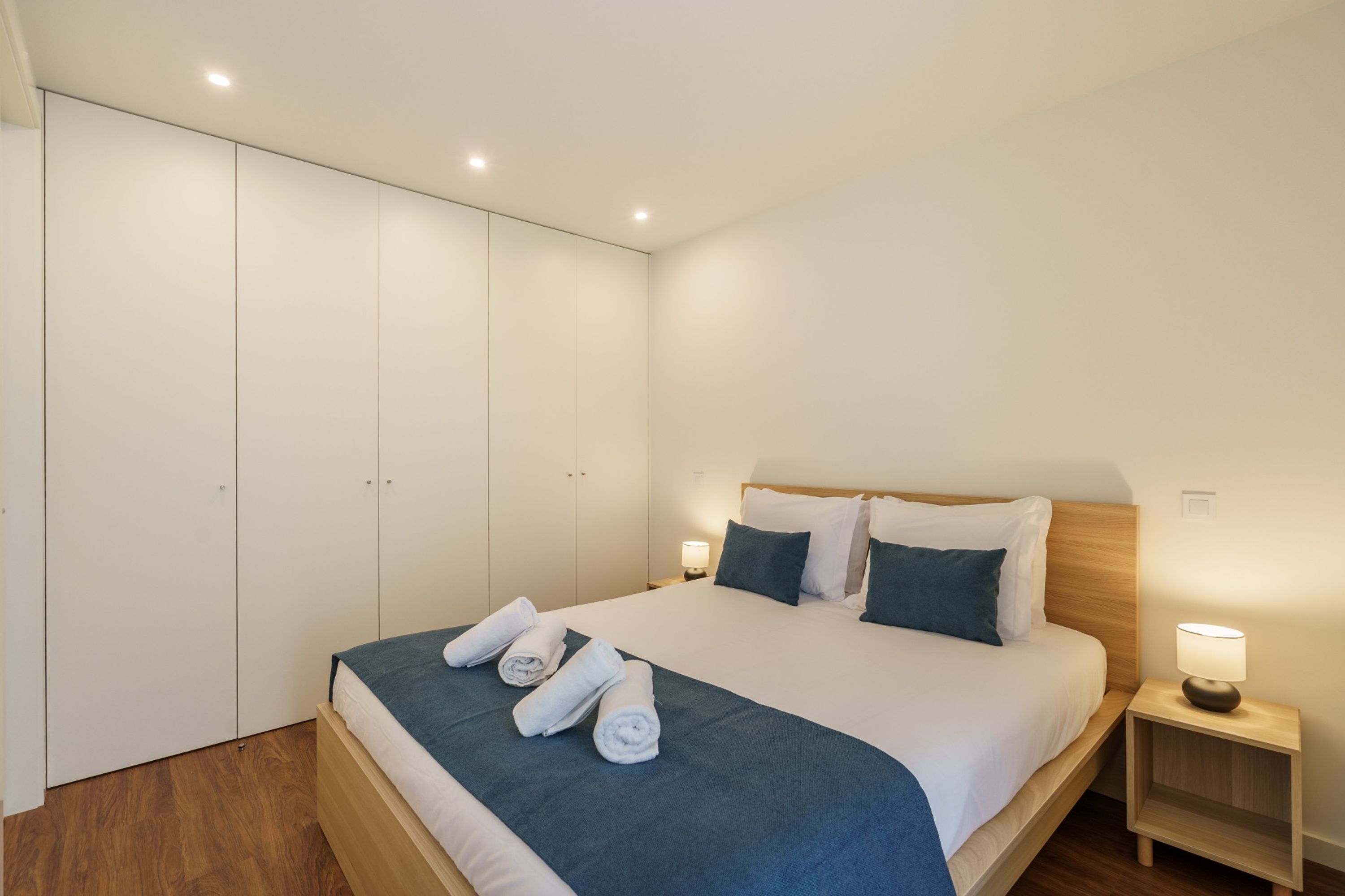 A neatly made bed with rolled towels, a wooden headboard, and a bedside table with a lamp.