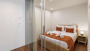 A modern hotel room with a large bed, a bedside table with a lamp, and a glass partition wall. - 196 Andrade Corvo Apartment by Minho s Guest (Braga)