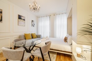 Ein modernes Hotelzimmer mit einem Glastisch, einer Couch, einem Bett und einem Chandelier.