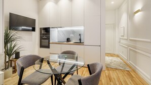 A modern kitchen with white cabinets, a built-in oven, and a marble backsplash. There is a glass dining table with two chairs. - Ch os Concept By Minhos Guest (Braga)