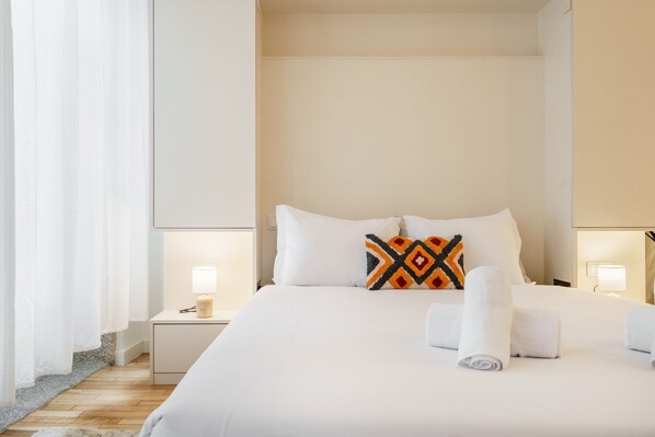 Ein Hotelzimmer mit einem großen Bett, weißen Leinentextilien, einem Zierkissen, zwei Nachttischlampen und einem Nachttisch mit Lampe.