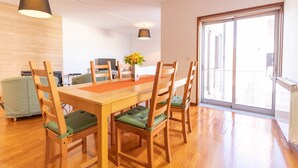 A dining area with a wooden table and chairs, a vase with flowers, and a view of the city through a large sliding glass door. - Machado s Lodge - Minho s Guest (Braga)