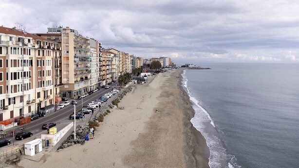 Paisagem costeira com edifícios altos, uma praia e um mar calmo.