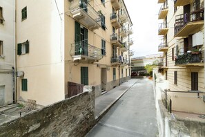 Una calle estrecha bordeada por edificios de varios pisos con balcones, un muro de hormigón y un cielo despejado.