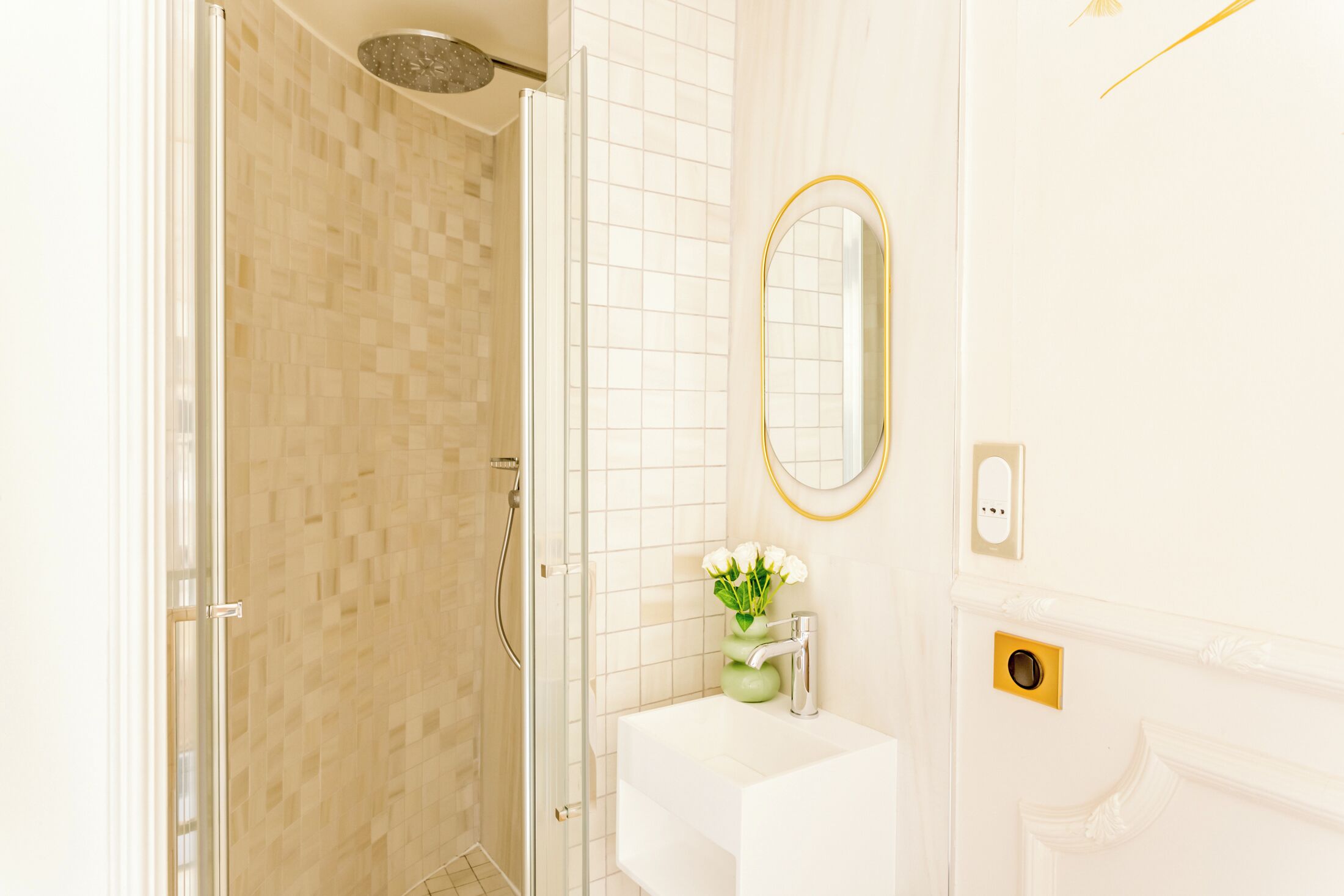 Une salle de bain dotée d’une douche à parois de verre, d’un lavabo blanc avec un robinet doré et d’un miroir avec un cadre doré.