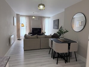 A modern living room with a sofa, TV, dining table, and a large mirror. - Toast Stays - The Oakley at Parsons House (Washington)