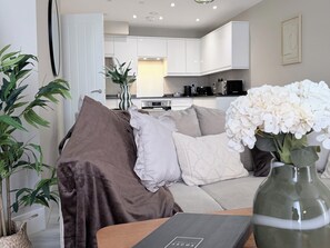 A modern living room with a sofa, cushions, a vase with flowers, and a view into the kitchen. - Toast Stays - The Oakley at Parsons House (Washington)