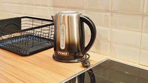 A Pyrex electric kettle on a kitchen counter with a black wire basket and a tiled backsplash. - Sleek Studio in Voula Center (Voula)