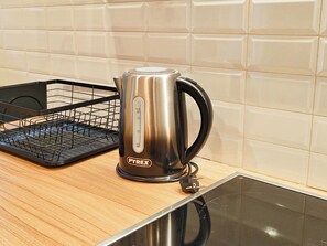 A Pyrex electric kettle on a kitchen counter with a black wire basket and a tiled backsplash. - Sleek Studio in Voula Center (Voula)