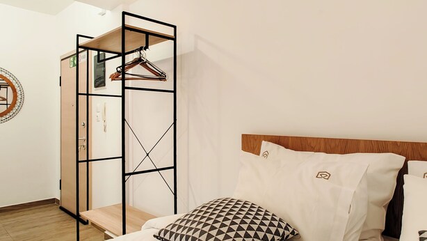A bedroom with a bed, a hanging clothes rack, a wooden bench, and a wall-mounted coat rack. - Sleek Studio in Voula Center (Voula)