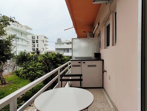 A balcony with a table and chairs, a small kitchenette, and a view of neighboring buildings. - Sleek Studio in Voula Center (Voula)
