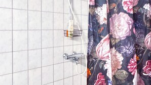 Un espacio de ducha con cortina floral, un cabezal de ducha manual y un grifo empotrado.