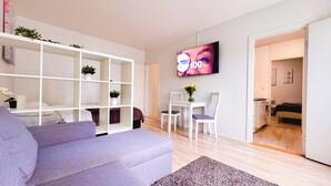 Una sala de estar moderna con un sofá, un aparador blanco, una mesa de comedor con sillas y un televisor montado en la pared.