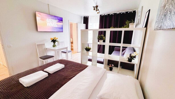 Habitación de hotel con cama, escritorio, silla y televisor mostrando 'SISTER WIVES'.