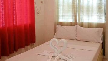 A hotel room with a bed, red curtains, beige curtains, and a heart-shaped towel arrangement.