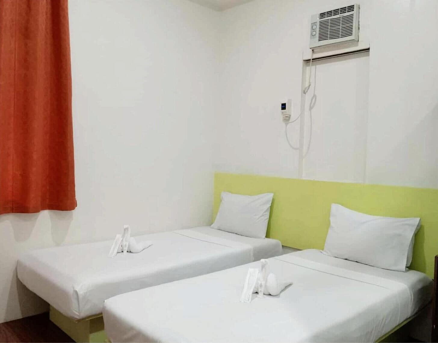 Une chambre d’hôtel avec deux lits simples, chacun doté de draps et d’oreillers blancs, d’une tête de lit verte et d’un climatiseur fixé au mur.