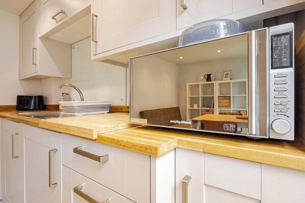 Una cocina moderna con microondas integrado, un lavamanos y una encimera de madera.