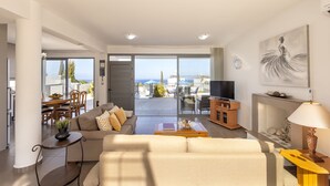 A modern living room with a sofa, coffee table, and TV, a dining area with chairs and a table, and a balcony with a view of the sea. - Lenias Sea View in Neo Chorio (Neo Chorio)