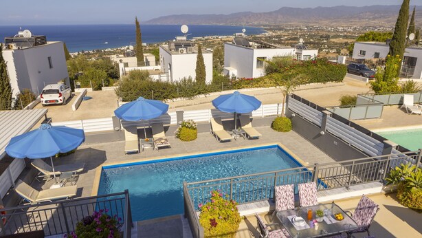A rooftop pool area with a view of the sea, lounge chairs, umbrellas, and a table with chairs. - Lenias Sea View in Neo Chorio (Neo Chorio)