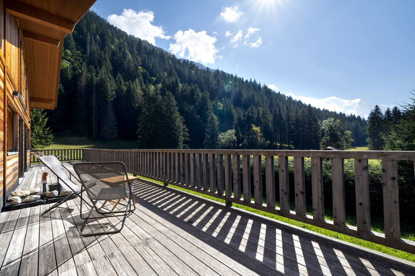 Un terrazzo in legno con poltrone relax e un parapetto che si affaccia su una montagna boscosa.
