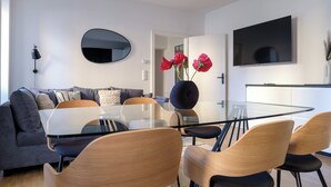 Una sala moderna con una mesa de comedor de vidrio, sofá gris y televisor de pantalla plana montado en la pared.