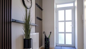 Un pasillo con una planta en maceta, un reloj, un radiador y una puerta con ventanal.