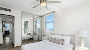 Ein modernes Hotelzimmer mit einem großen Bett, einem Deckenventilator, einem Fenster mit Blick und einer Schiebetür zu einem weiteren Raum.