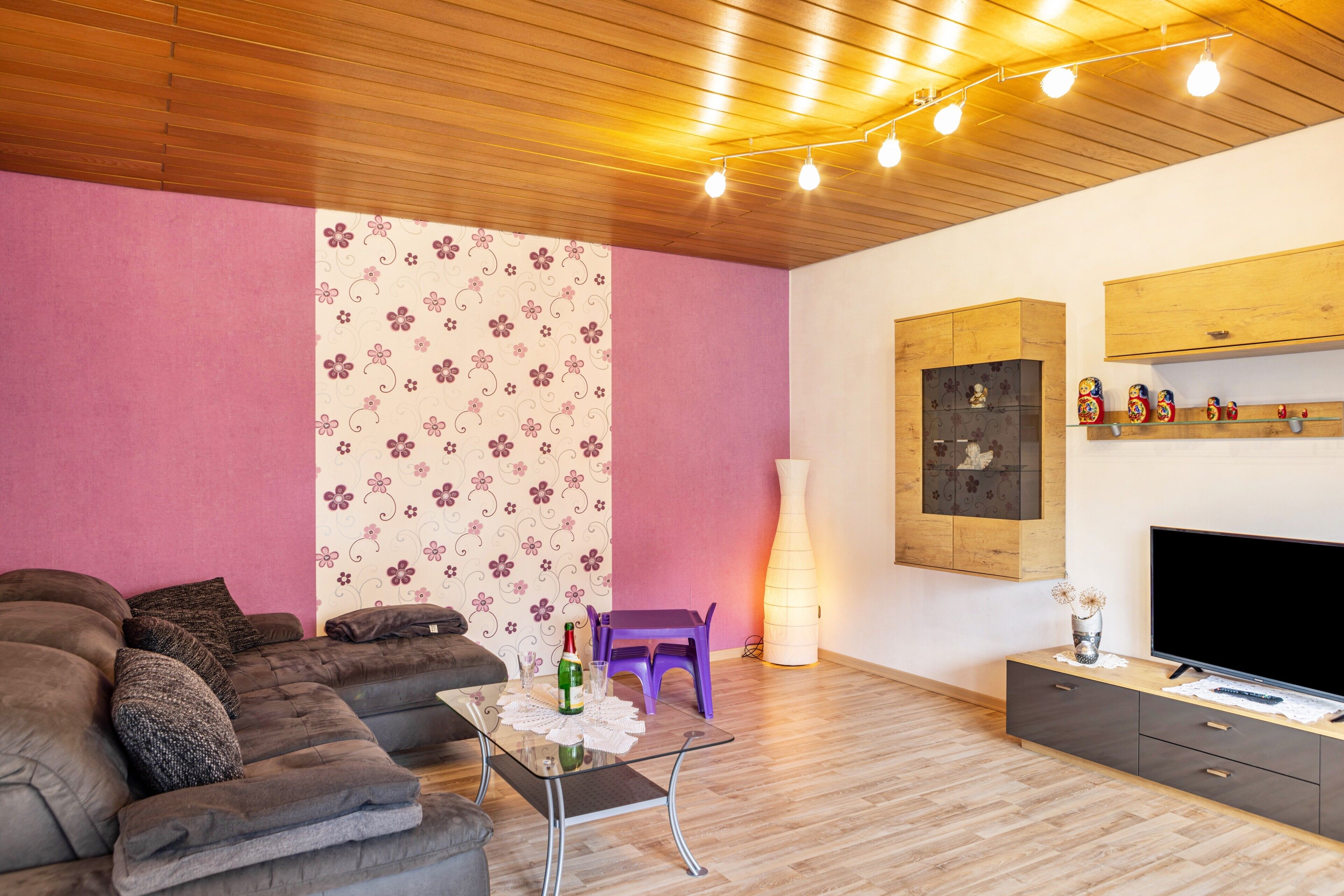 Ein modernes Wohnzimmer mit einer Couch, einem Glastisch, einem Flachbildfernseher, einem Holzschrank und einer dekorativen Leuchte.